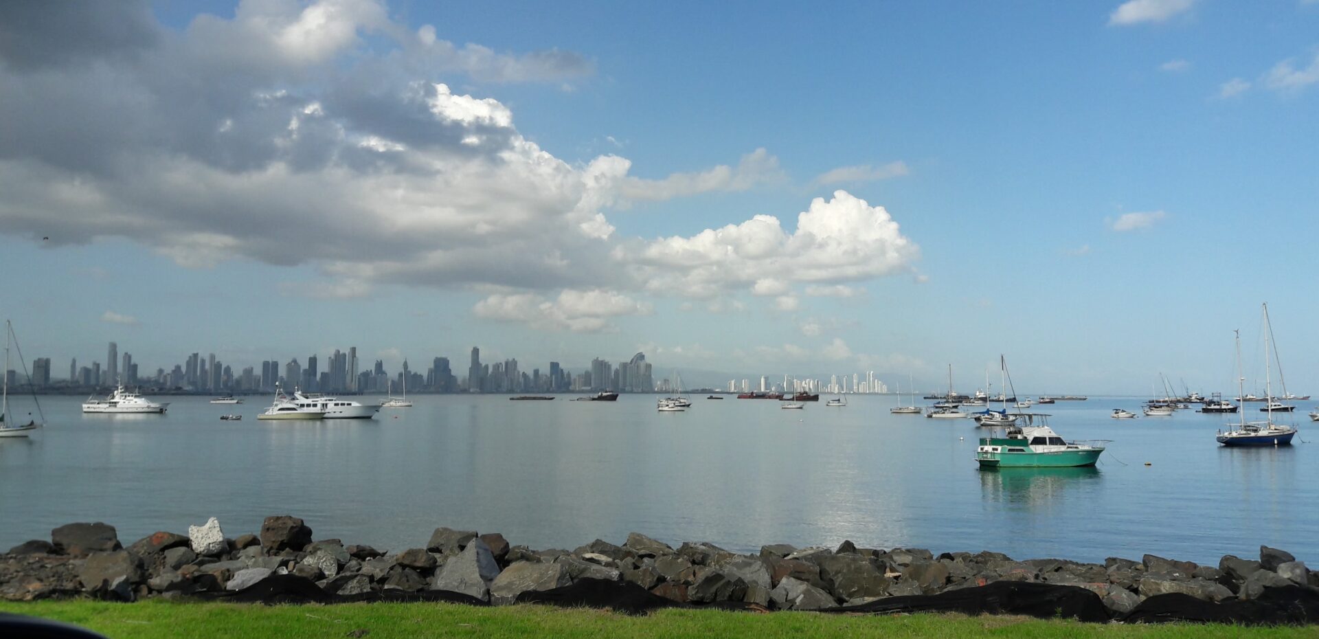 Ruhige Bucht mit Segelbooten, Motorbooten und Skyline im Hintergrund unter blauem Himmel.